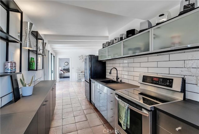 kitchen with dark countertops, backsplash, stainless steel electric range, and a sink