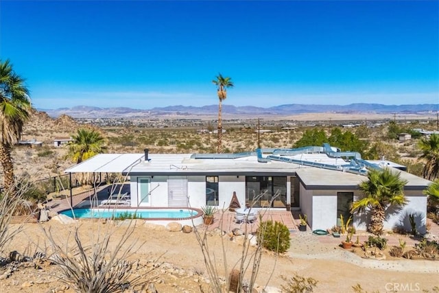 rear view of house featuring an outdoor pool, roof mounted solar panels, a mountain view, and stucco siding