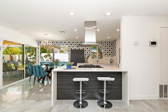 kitchen with a kitchen bar, decorative backsplash, kitchen peninsula, stainless steel gas cooktop, and island range hood