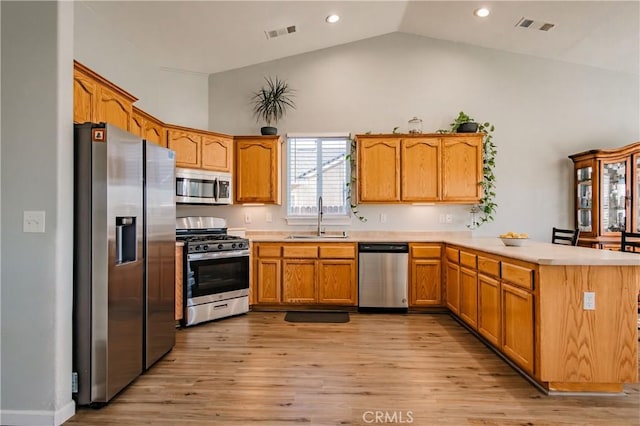 kitchen featuring kitchen peninsula, stainless steel appliances, sink, high vaulted ceiling, and light hardwood / wood-style floors