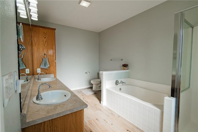 bathroom with tiled bath, vanity, wood-type flooring, and toilet