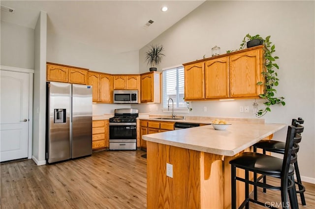 kitchen featuring light wood-type flooring, kitchen peninsula, sink, and appliances with stainless steel finishes