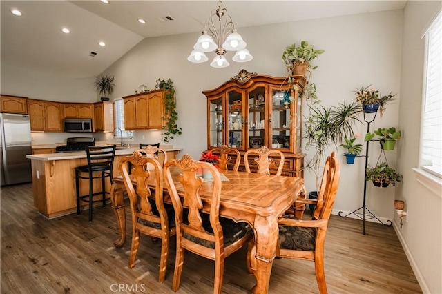 dining area featuring hardwood / wood-style flooring, a chandelier, sink, and vaulted ceiling