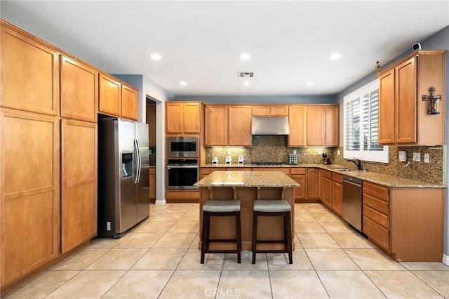 kitchen featuring appliances with stainless steel finishes, light stone counters, a breakfast bar, sink, and a center island