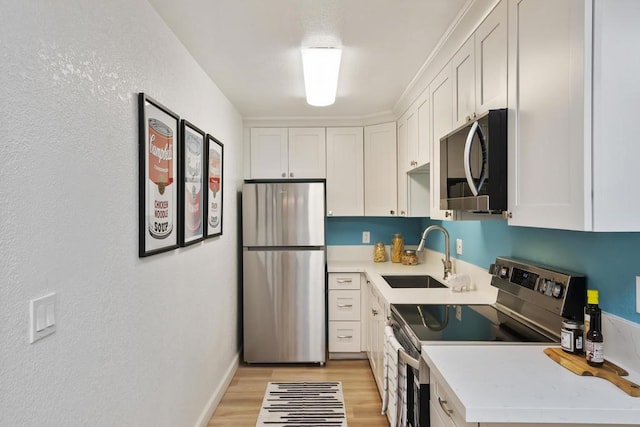 kitchen with stainless steel appliances, white cabinetry, sink, and light hardwood / wood-style floors