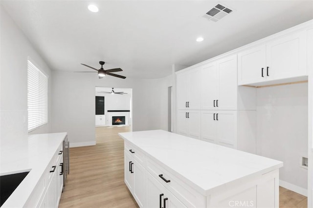 kitchen with light wood-type flooring, ceiling fan, white cabinetry, and a kitchen island