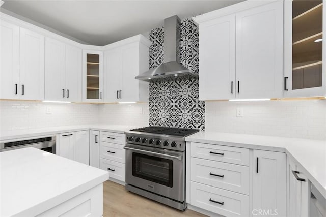 kitchen with appliances with stainless steel finishes, wall chimney exhaust hood, white cabinetry, decorative backsplash, and light hardwood / wood-style floors