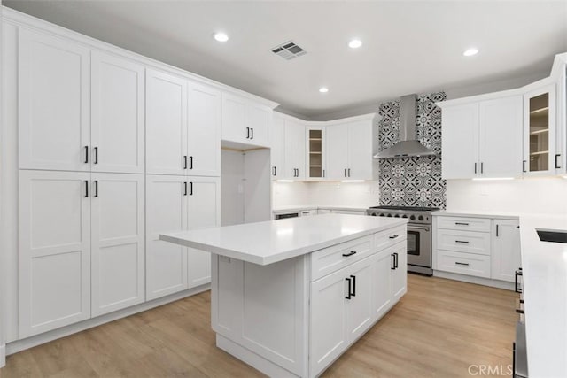 kitchen featuring backsplash, wall chimney range hood, white cabinetry, light hardwood / wood-style flooring, and stainless steel range