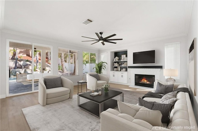 living room with ornamental molding, a fireplace, light hardwood / wood-style flooring, and built in shelves