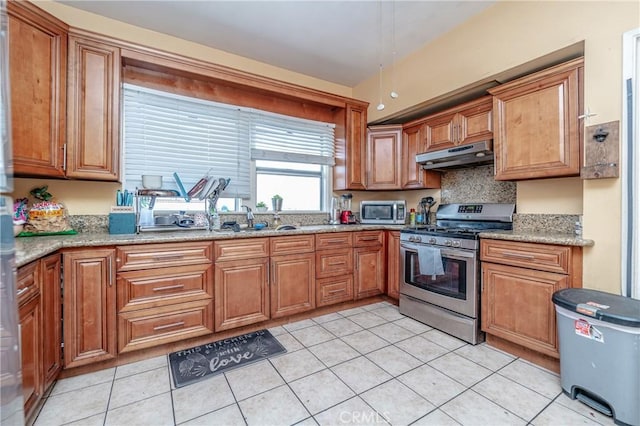 kitchen with light stone countertops, appliances with stainless steel finishes, light tile patterned floors, and sink