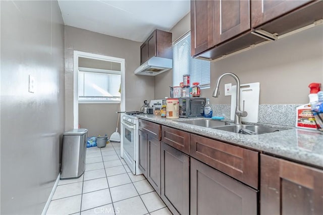 kitchen featuring sink, white gas range oven, light stone countertops, dark brown cabinets, and light tile patterned flooring