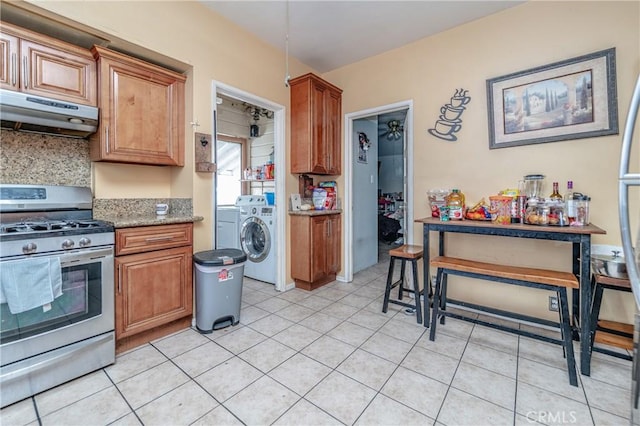 kitchen with stainless steel gas range oven, backsplash, light stone countertops, light tile patterned floors, and range hood