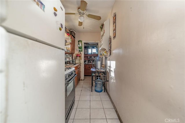 kitchen with black range, white fridge, light tile patterned floors, and ceiling fan