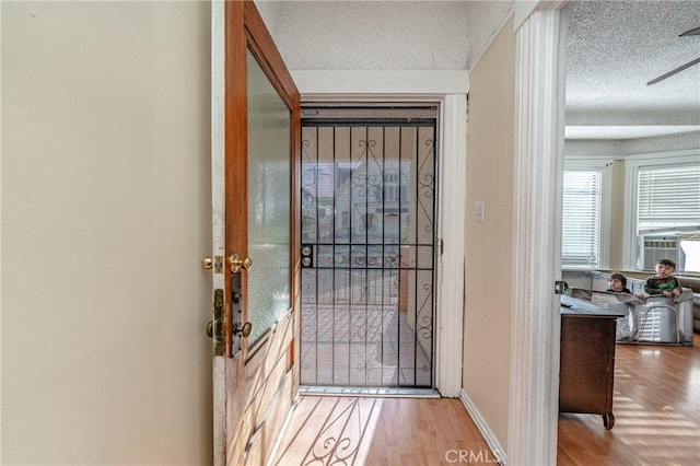 doorway to outside with ceiling fan, light wood-type flooring, and a textured ceiling