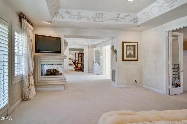 unfurnished living room featuring a multi sided fireplace, light colored carpet, and a tray ceiling