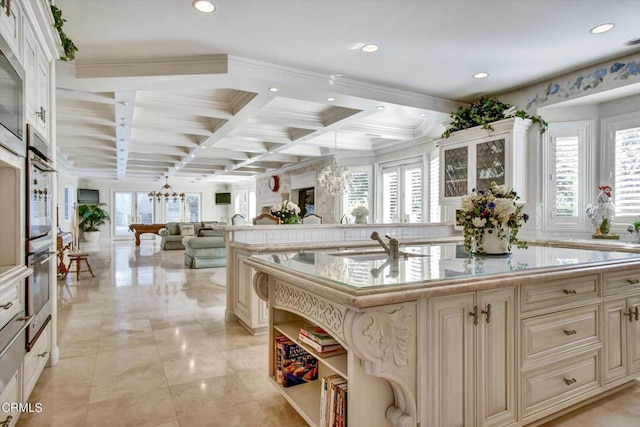 kitchen featuring beam ceiling, sink, a kitchen island with sink, and cream cabinets