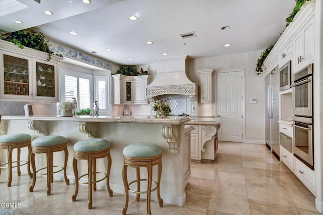 kitchen with tasteful backsplash, white cabinetry, a kitchen bar, and custom range hood