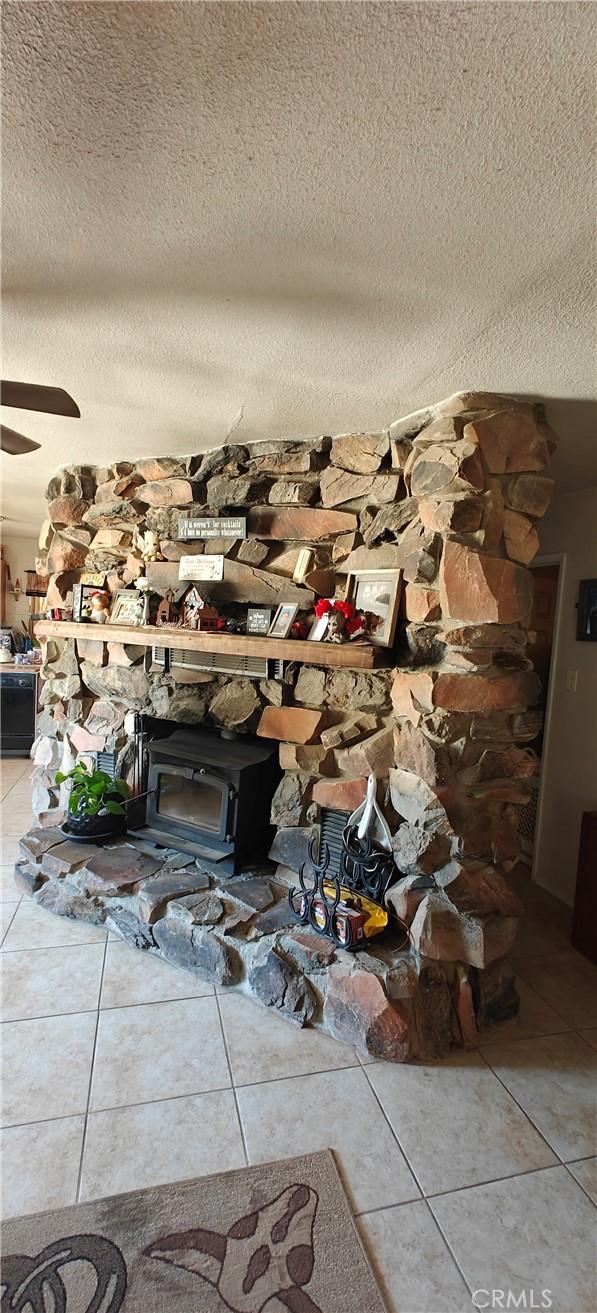 interior details featuring ceiling fan, a wood stove, and a textured ceiling