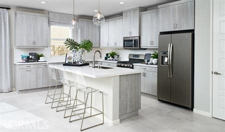 kitchen featuring sink, hanging light fixtures, stainless steel appliances, a breakfast bar, and a center island with sink