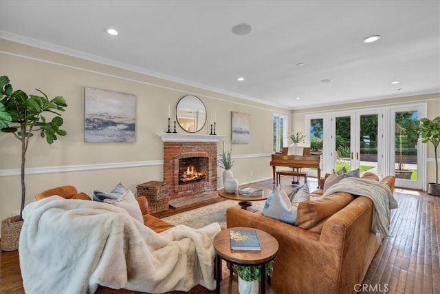 living room with hardwood / wood-style flooring, french doors, ornamental molding, and a brick fireplace