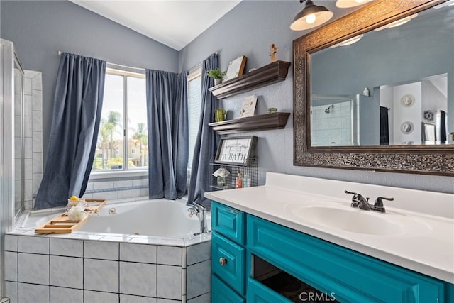 bathroom with vaulted ceiling, a healthy amount of sunlight, tiled bath, and vanity