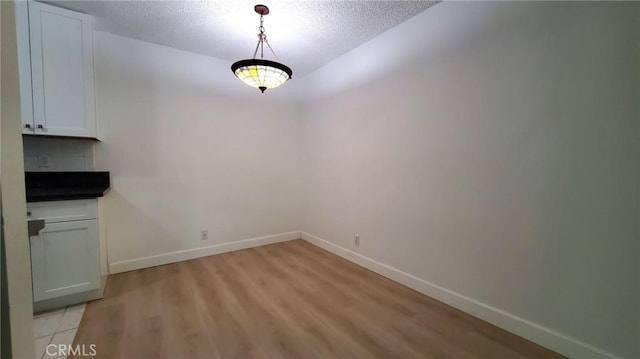 unfurnished dining area with light wood-type flooring and a textured ceiling