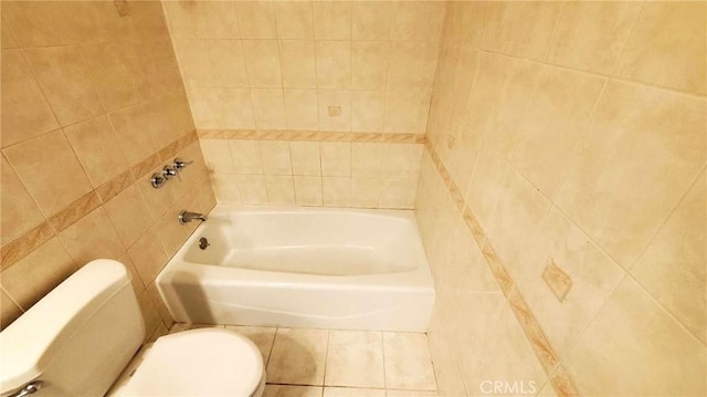 bathroom featuring tile patterned flooring, a bath, toilet, and tile walls