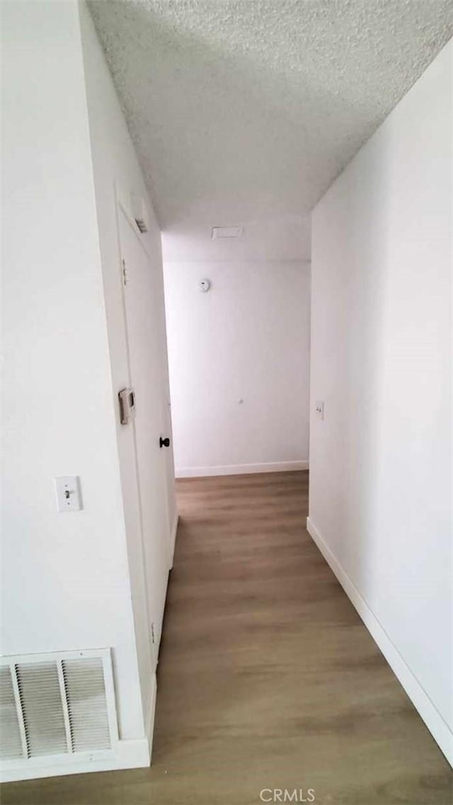 corridor with a textured ceiling and hardwood / wood-style flooring