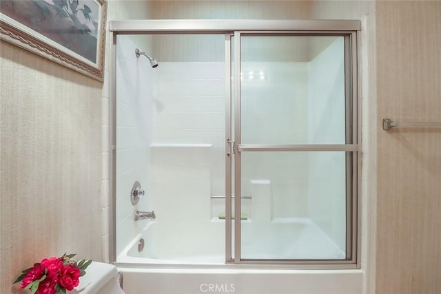 bathroom featuring toilet and bath / shower combo with glass door