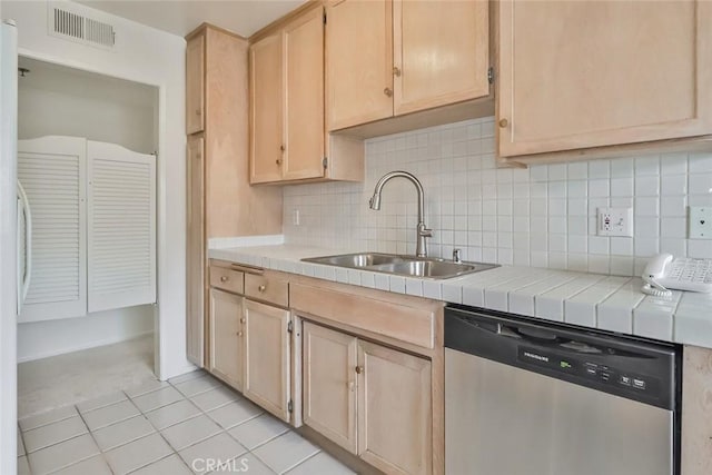 kitchen with light brown cabinetry, backsplash, stainless steel dishwasher, sink, and tile counters