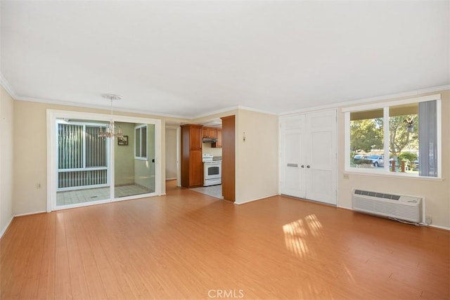 unfurnished living room with an AC wall unit, an inviting chandelier, ornamental molding, and light wood-type flooring