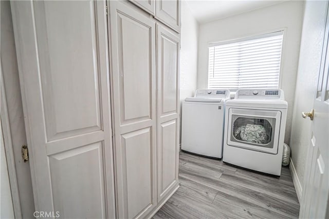 laundry area featuring washing machine and dryer, cabinets, and light wood-type flooring