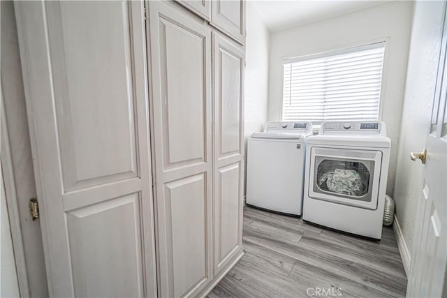 laundry area featuring light wood-style floors, separate washer and dryer, and cabinet space