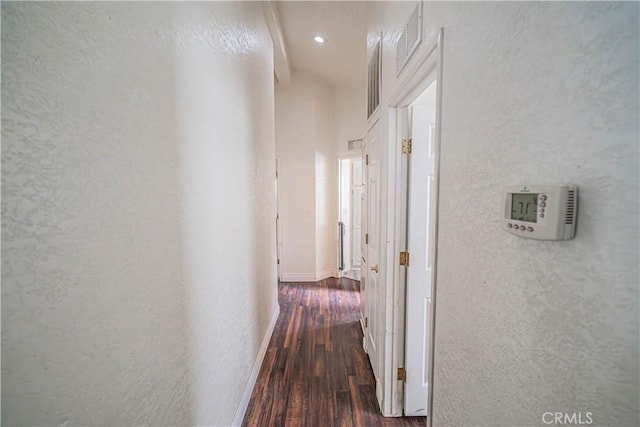 hallway featuring dark wood-style floors, visible vents, and a textured wall