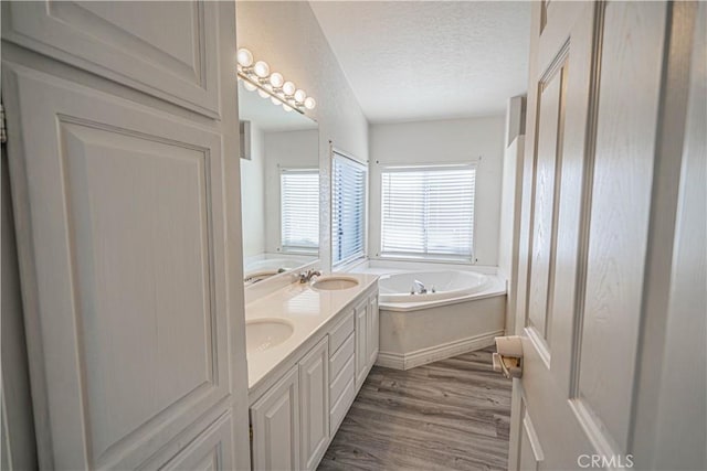full bathroom with wood finished floors, a textured ceiling, double vanity, a sink, and a garden tub