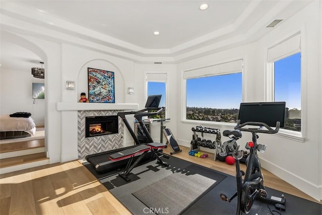 workout area with a raised ceiling, a fireplace, and hardwood / wood-style floors