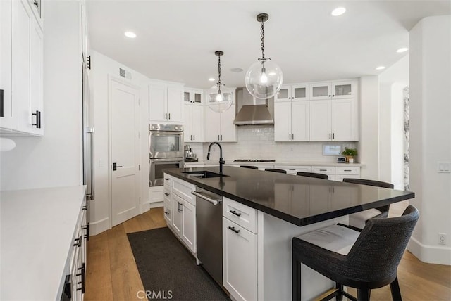 kitchen with sink, wall chimney range hood, wood-type flooring, a center island with sink, and white cabinetry