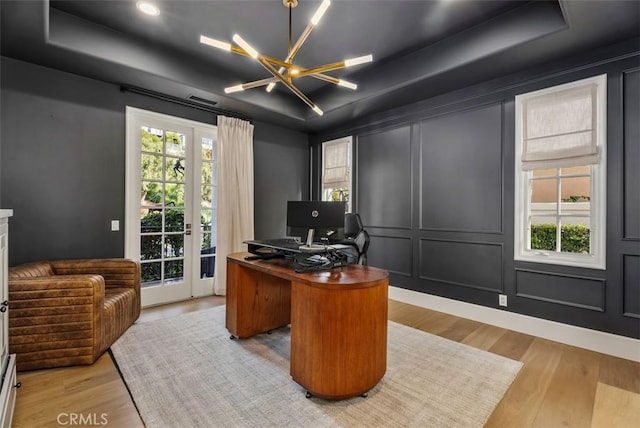 office area with a raised ceiling, light hardwood / wood-style floors, an inviting chandelier, and plenty of natural light