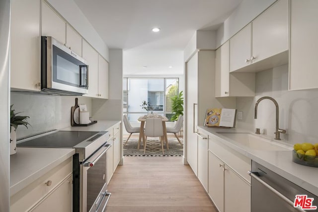 kitchen featuring appliances with stainless steel finishes, light wood-type flooring, tasteful backsplash, sink, and white cabinets