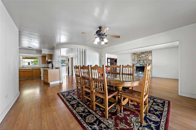 dining area with a fireplace, light wood-type flooring, ceiling fan, and sink