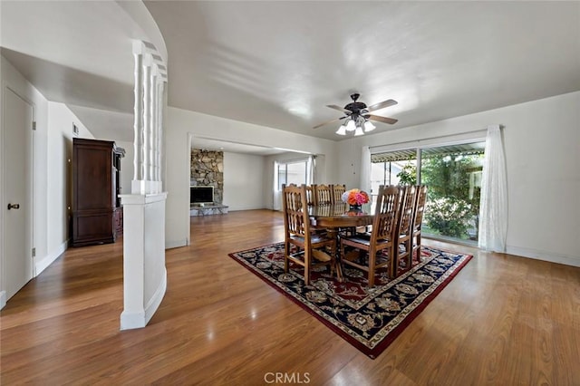 dining area with decorative columns, a stone fireplace, ceiling fan, and hardwood / wood-style flooring