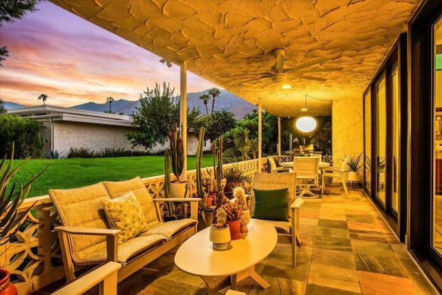 patio terrace at dusk with a mountain view, a yard, and ceiling fan