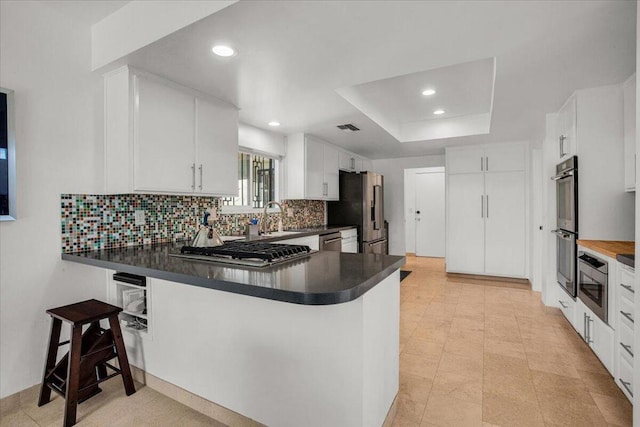 kitchen featuring kitchen peninsula, backsplash, appliances with stainless steel finishes, white cabinetry, and sink