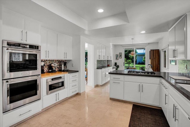 kitchen featuring a tray ceiling, kitchen peninsula, stainless steel appliances, white cabinets, and decorative backsplash