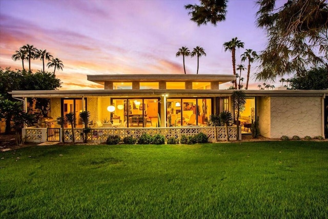 back house at dusk featuring covered porch and a lawn