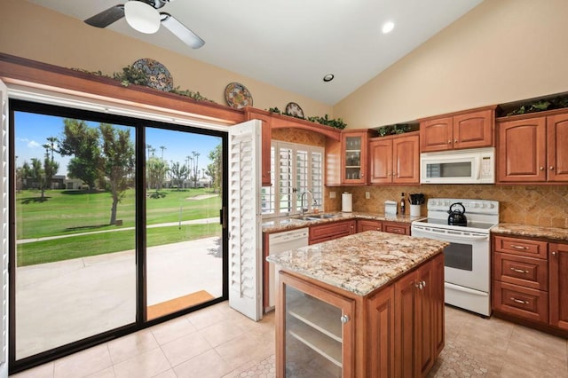 kitchen with decorative backsplash, light stone counters, white appliances, sink, and a kitchen island