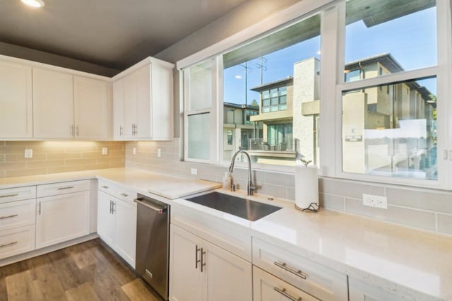 kitchen with dark wood-type flooring, a sink, backsplash, stainless steel dishwasher, and white cabinetry