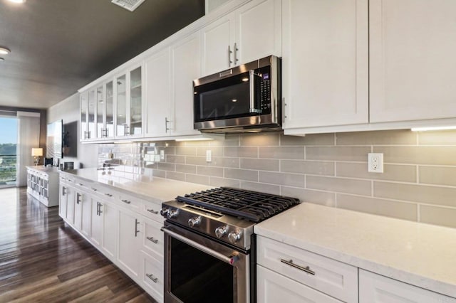 kitchen featuring dark wood-type flooring, backsplash, white cabinetry, appliances with stainless steel finishes, and glass insert cabinets