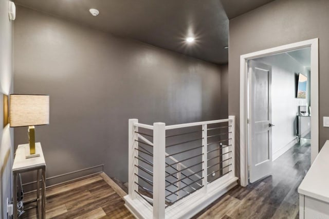 hall with an upstairs landing, recessed lighting, dark wood-type flooring, and baseboards