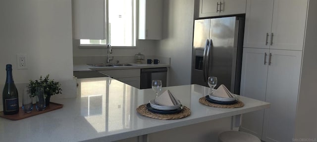 kitchen with white cabinetry, sink, dishwasher, a kitchen breakfast bar, and stainless steel fridge with ice dispenser